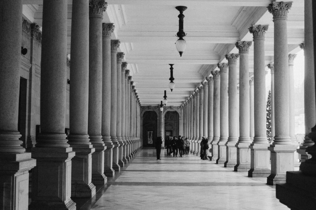 Black and white image showcasing grand architectural columns with people walking beneath.